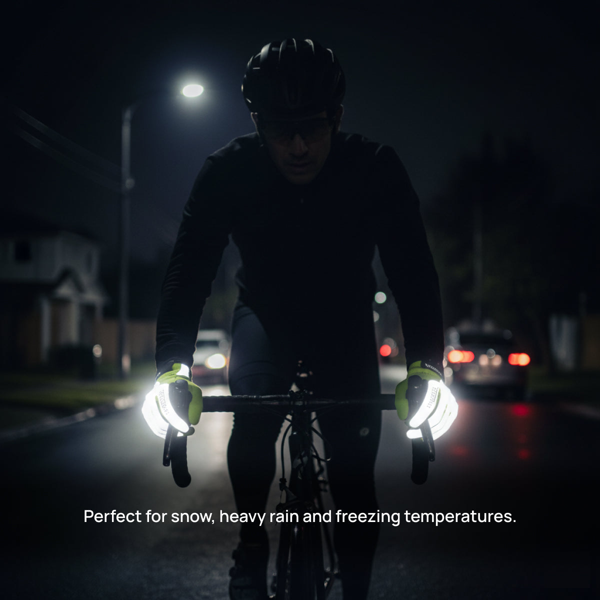 Male cyclist riding at night wearing neon yellow reflective thermal gloves on wet dark road